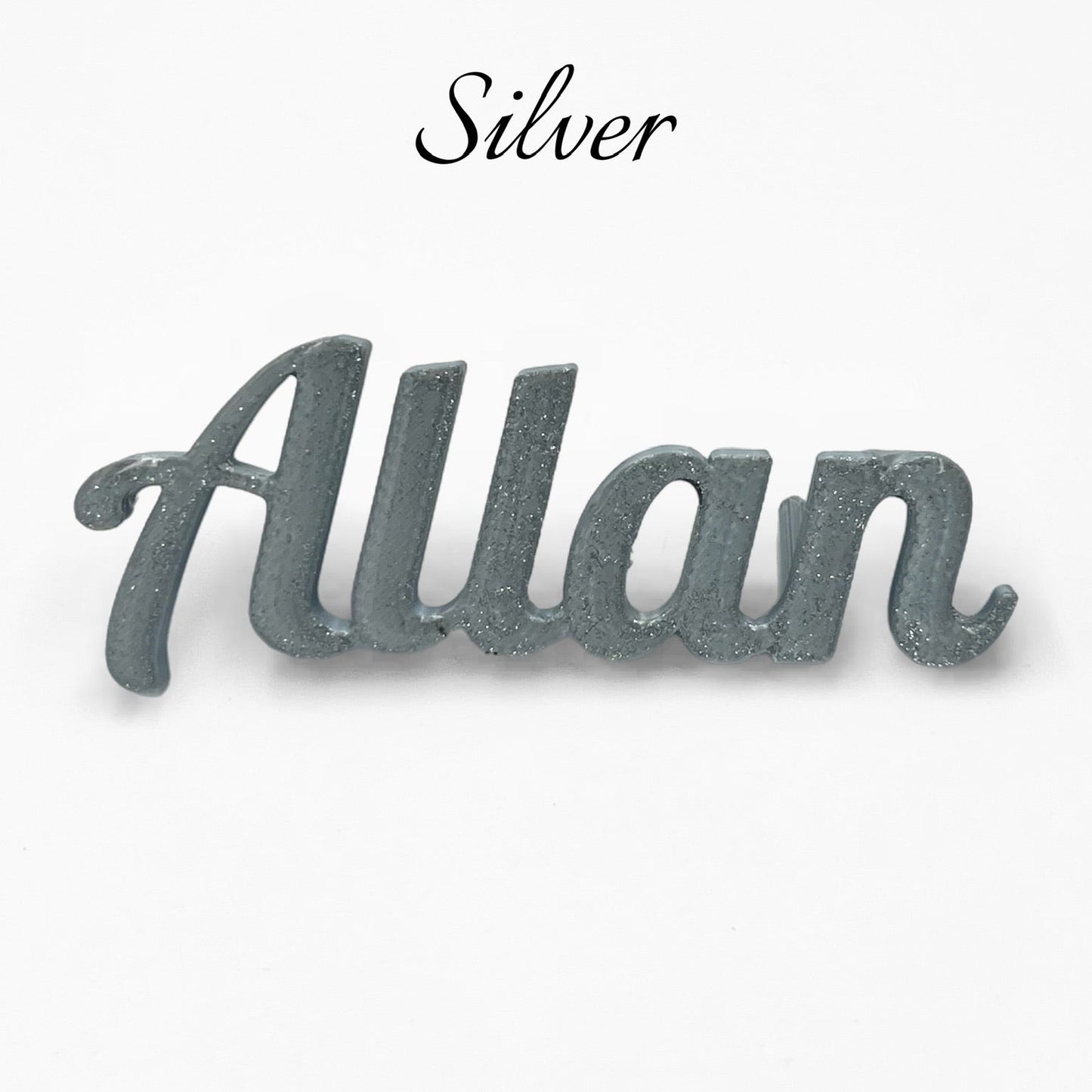A close-up studio shot of a silver 3D printed personalised name plate spelling "Allan" on a plain white background. The word "Silver" is written in a cursive font above the name.

