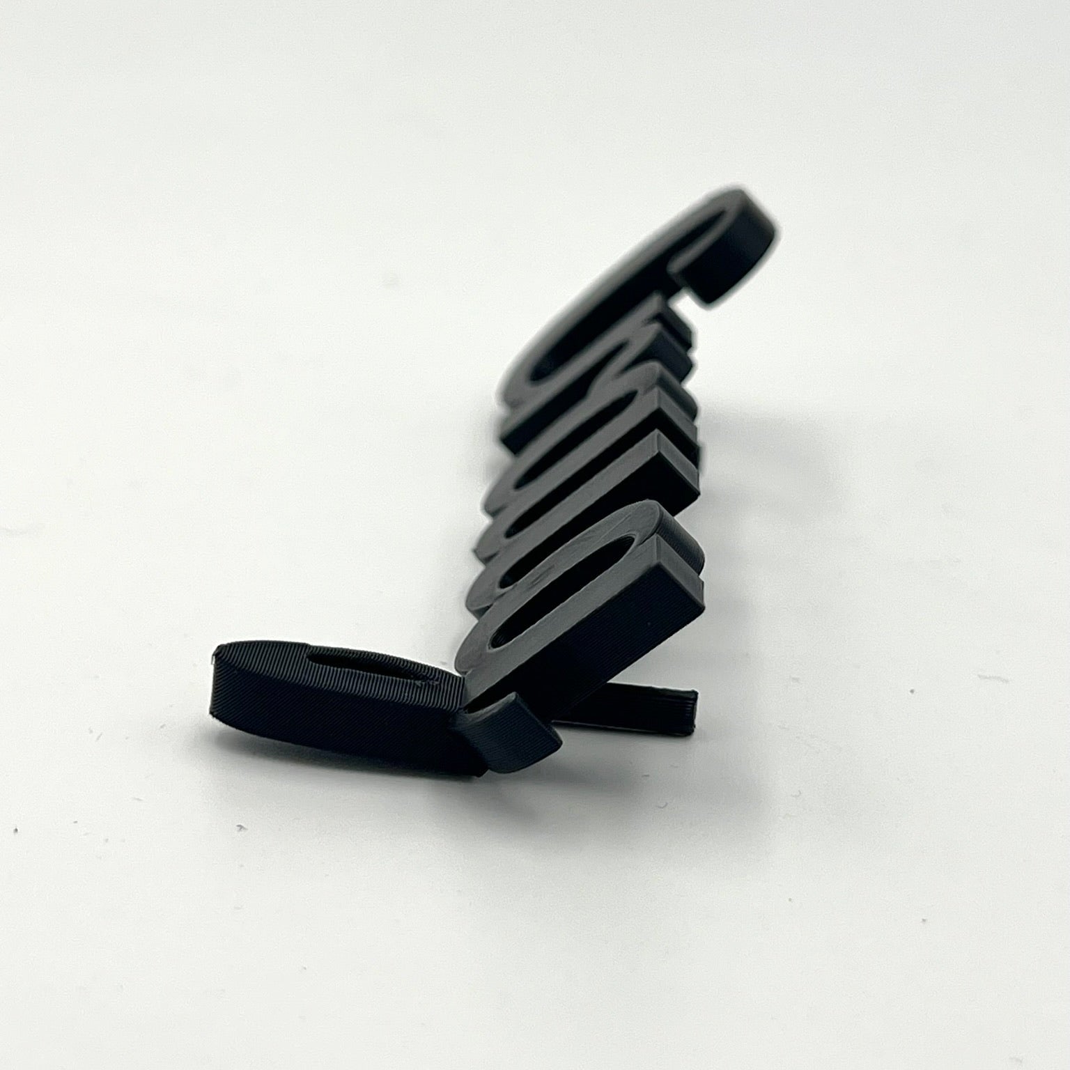 A side-view close-up of a black 3D printed personalised place name spelling "Craig" resting on a plain white surface. The three-dimensional nature of the lettering and its thickness are visible.